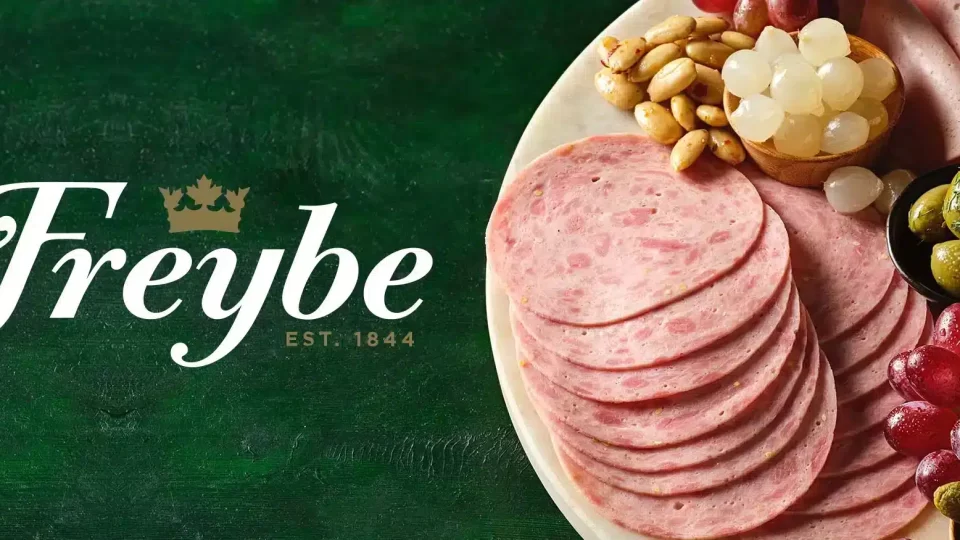 Freybe logo next to a plate of fresh goods delivered by Trappers Transport. The plate contains sliced ham, olives, grapes, and pickled pearl onions.