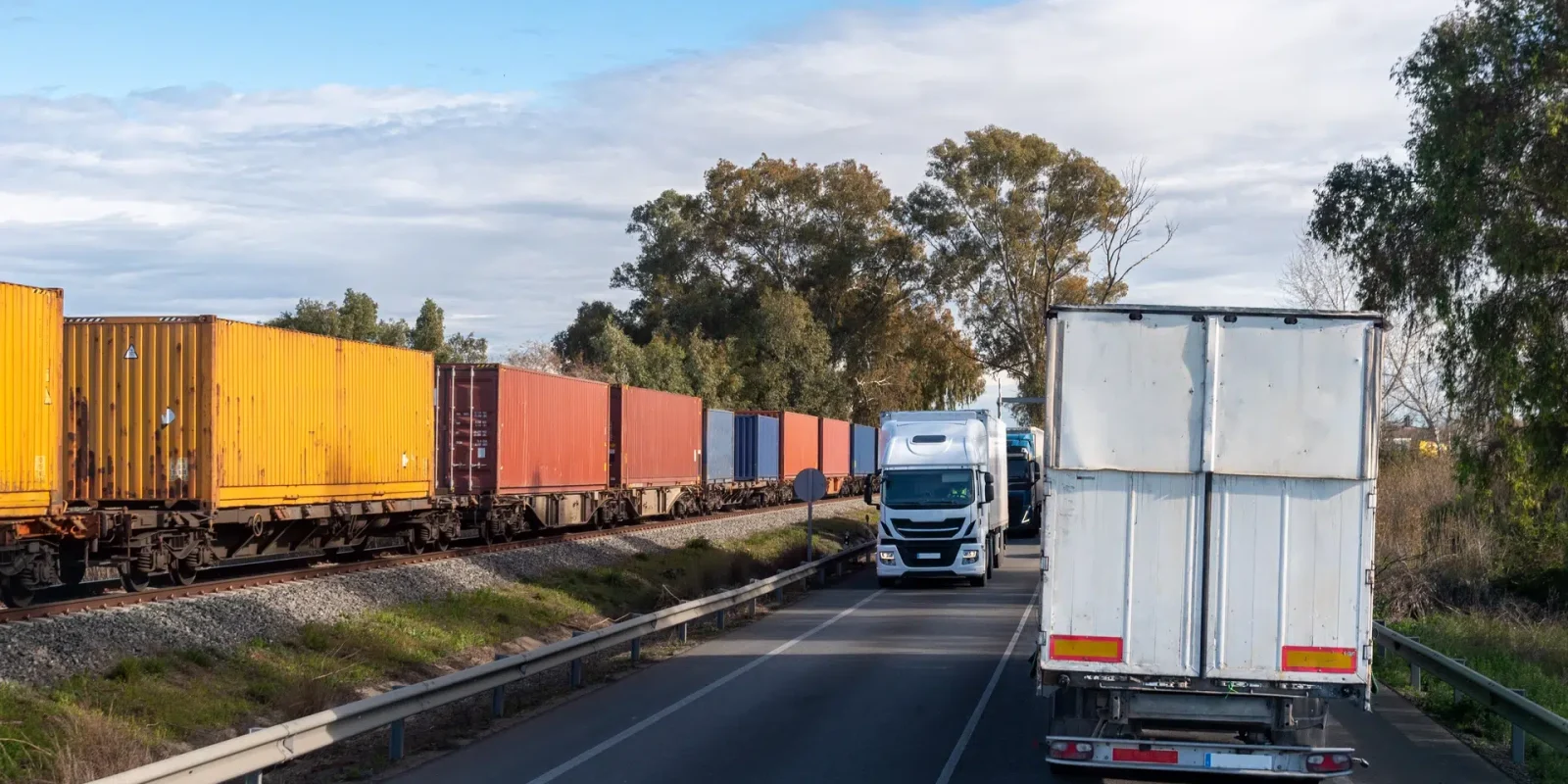 Train tracks and a road side by side. Intermodal containers are being carried by train and by truck.
