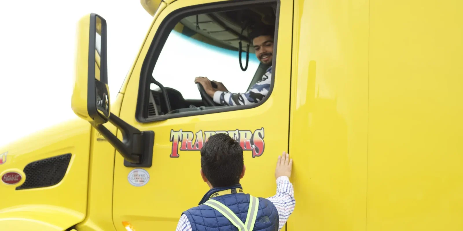 trappers-transport-container-drayage-drivers-chatting Two Trappers Transport employees talking. One is sitting at the wheel of a truck used for drayage of shipping containers.