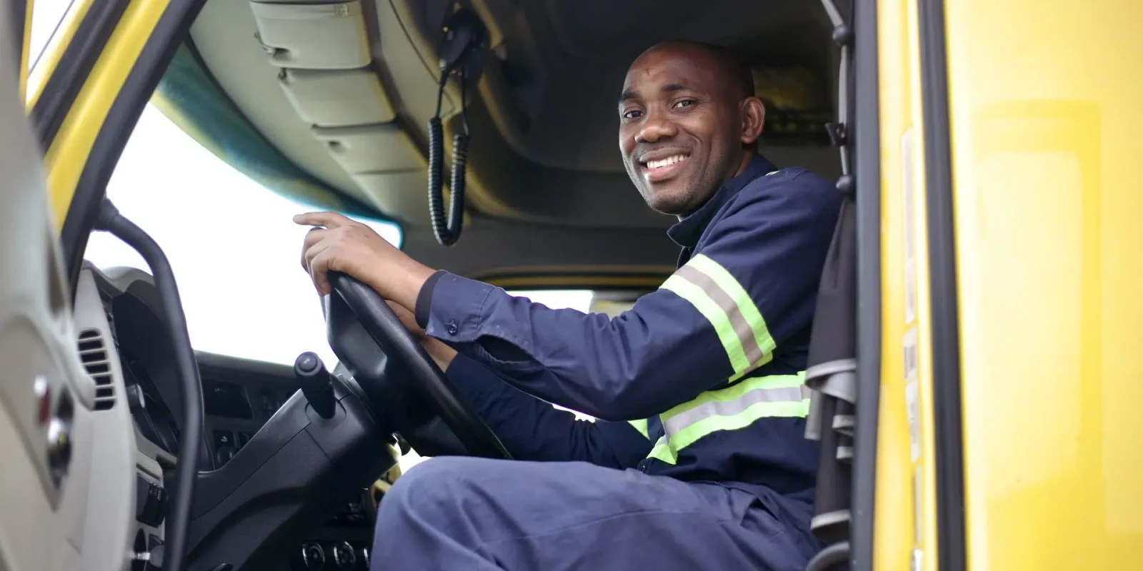 A Trappers Transport truck driver sitting in the cab of a truck, smiling.