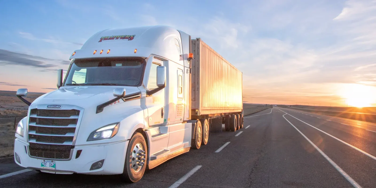 A Trappers Transport truck driving down a Manitoba highway at sunset.